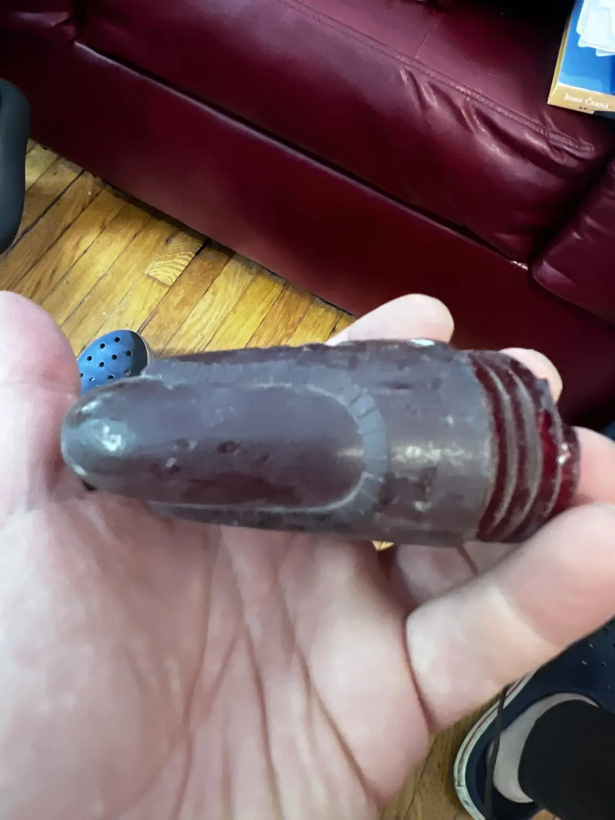 A hand holds a dark, translucent, cylindrical object with ridges and a worn, slightly melted appearance, resembling a melted…