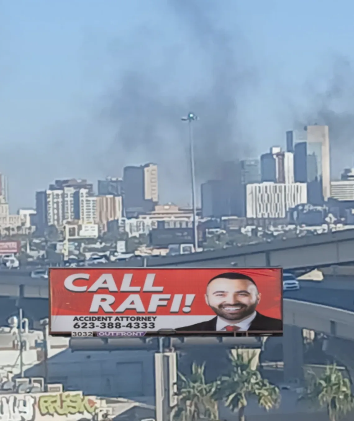 A large billboard advertising an accident attorney named Rafi, featuring his smiling photo and phone number, is positioned…