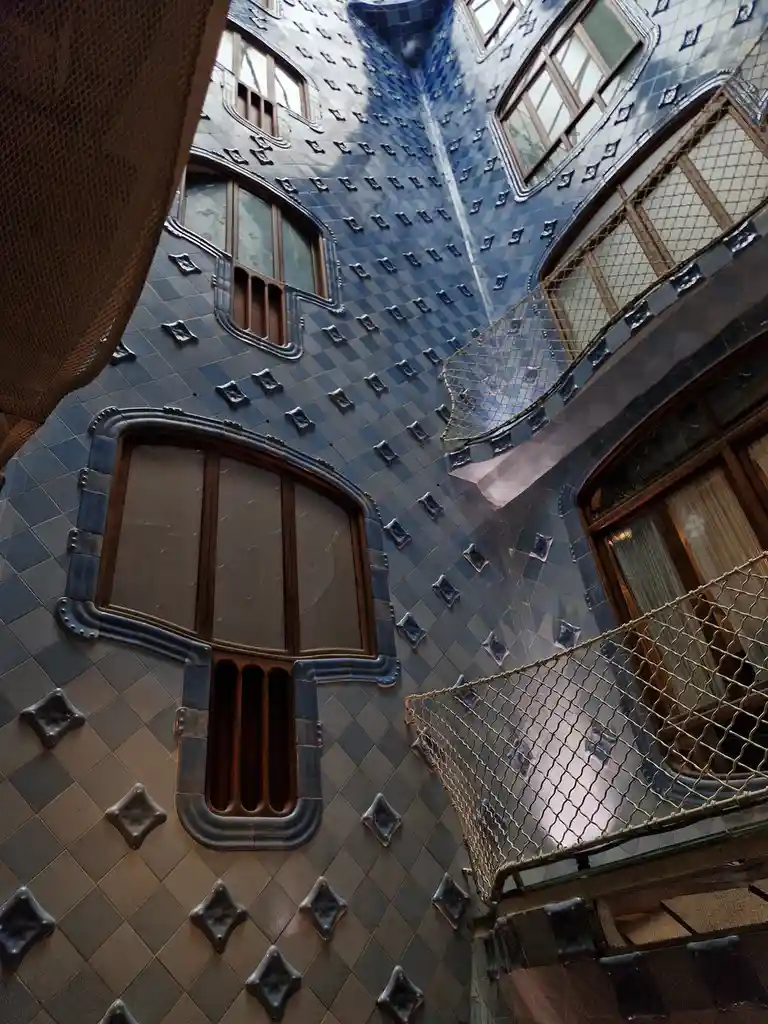 this is a photo of the interior courtyard of the casa batlló in barcelona, featuring its distinctive blue and gray tiled…