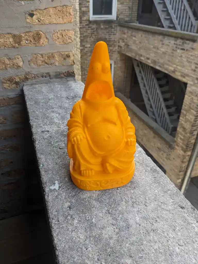 A bright orange, 3D-printed statue of the cartoon character Patrick Star from SpongeBob SquarePants, sitting cross-legged in…
