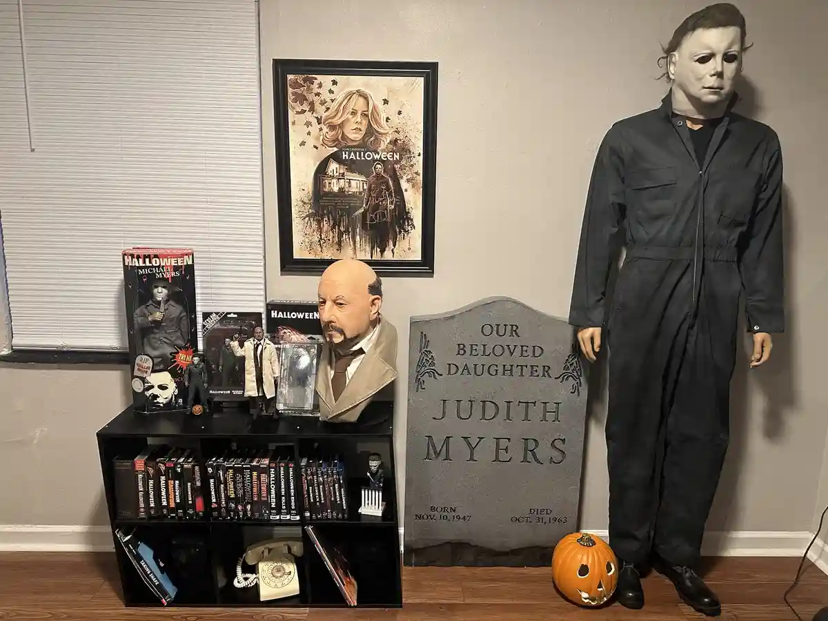 A room decorated with Halloween memorabilia, featuring a full-sized Michael Myers costume standing next to a tombstone that…