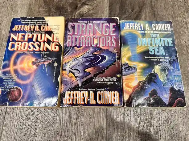 Three well-worn science fiction paperback books by Jeffrey A. Carver, titled 'Neptune Crossing' (Volume One), 'Strange…