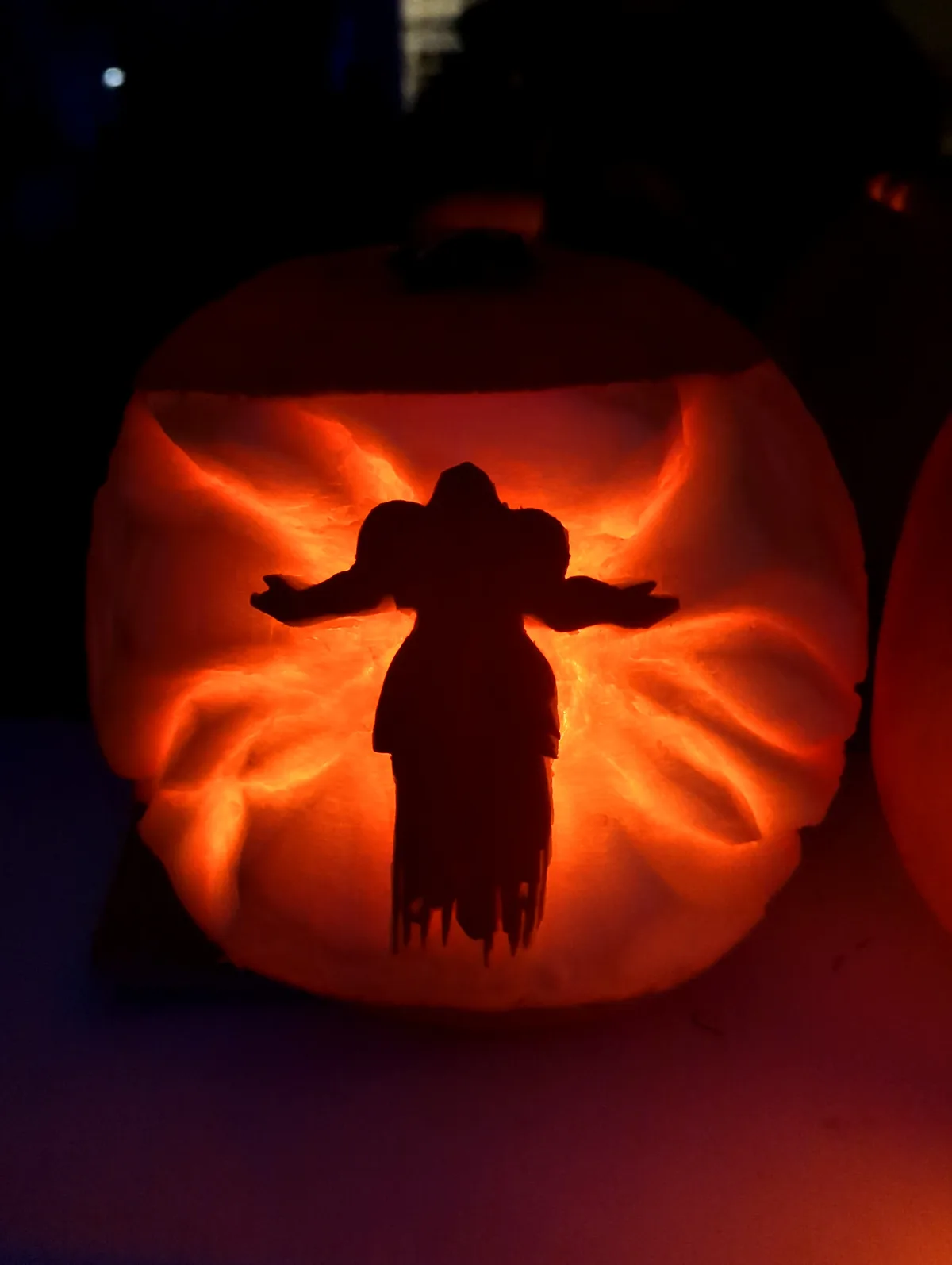 A carved pumpkin with an internal light source illuminates a silhouette of a character with outstretched arms and a flowing…