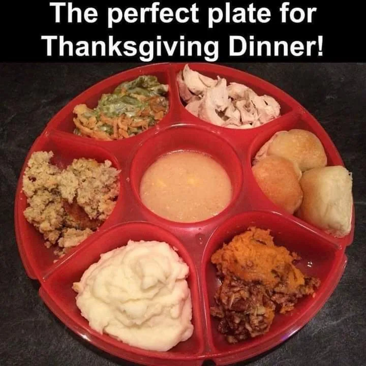 A red, circular, compartmentalized plate holds six traditional Thanksgiving foods: green bean casserole, turkey, cornbread…