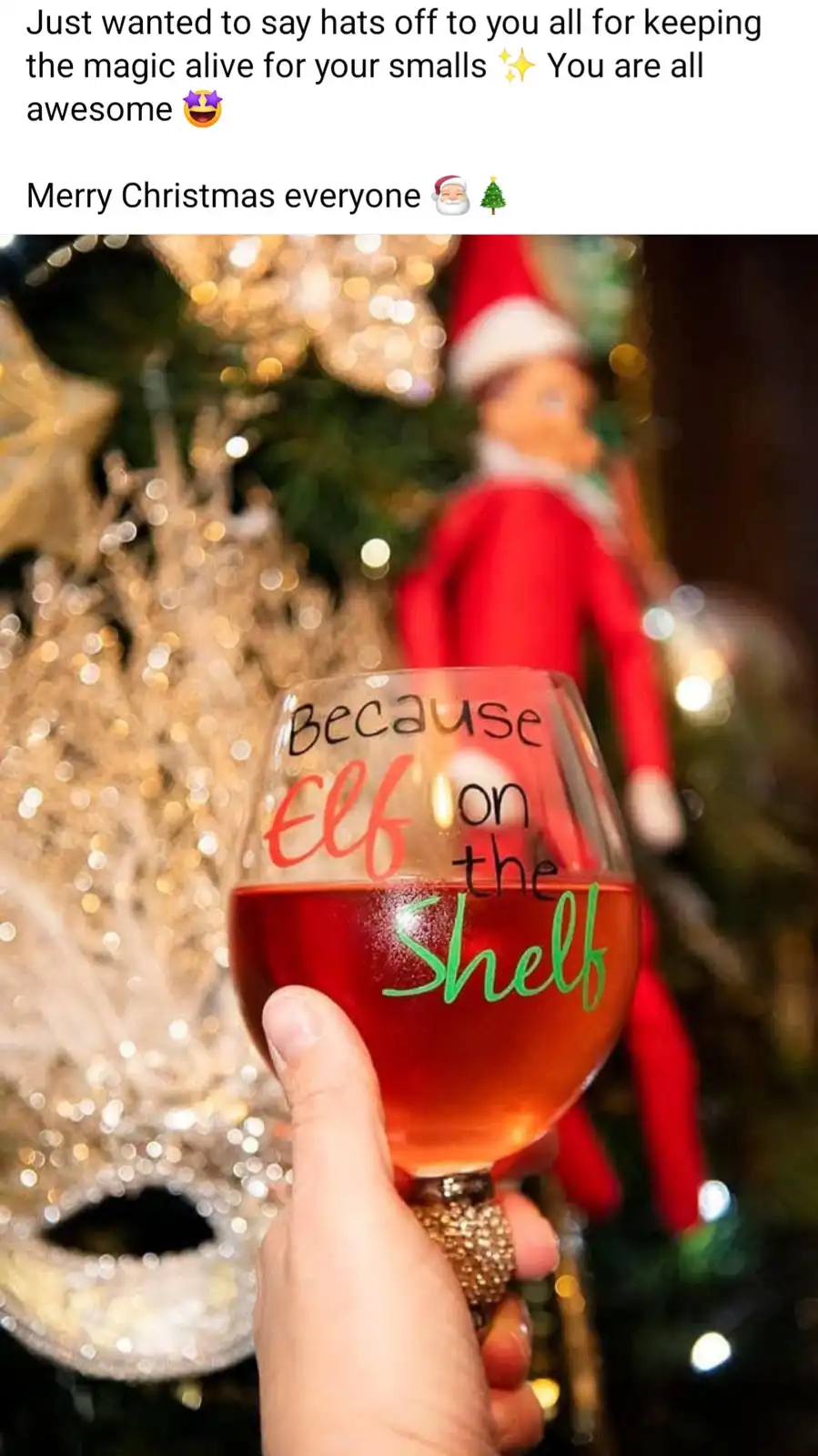 A hand holds a wine glass filled with red liquid, the glass labeled 'Because Elf on the Shelf' in colorful lettering. In the…