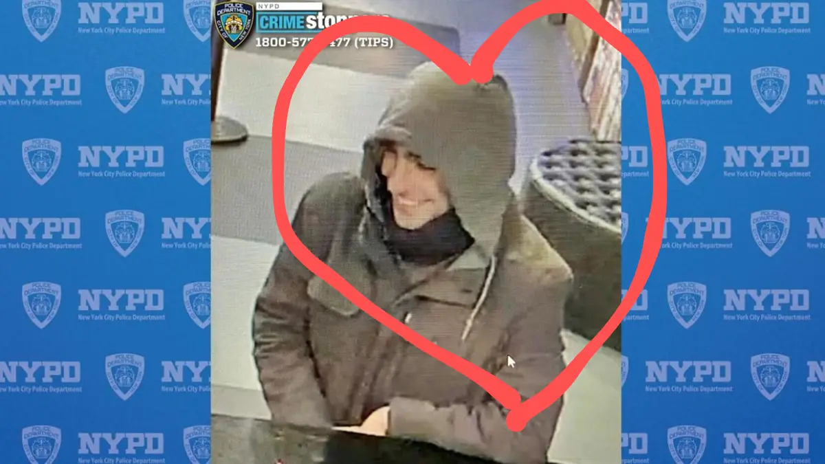 A grainy security camera image of a person in a dark hoodie and jacket, smiling, is overlaid with a large red heart drawn…