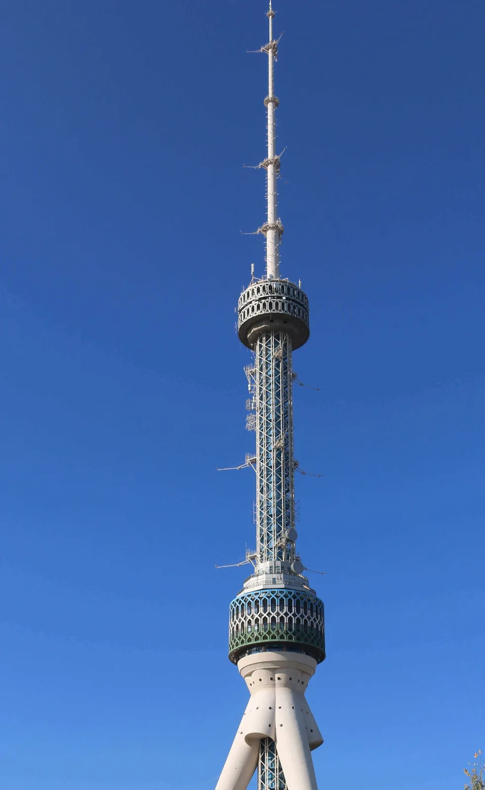 A tall, white telecommunications tower with a lattice structure and antenna array stands against a clear blue sky. The tower…