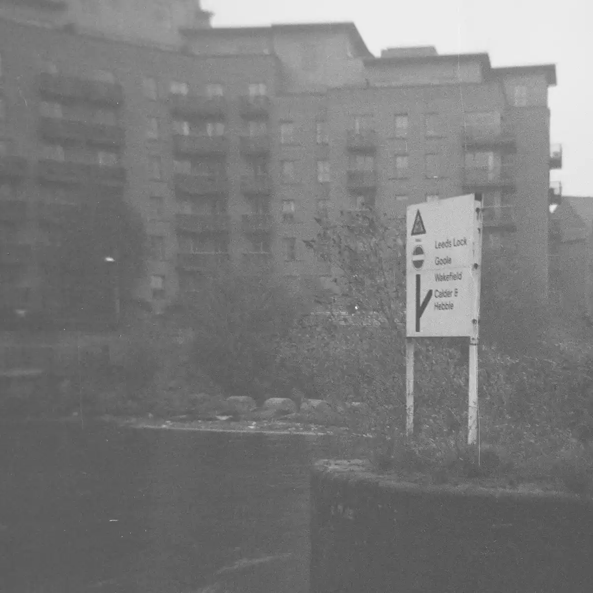 A grainy black-and-white photo shows a weathered road sign with directional arrows pointing to Leeds Lock, Goole, Wakefield…