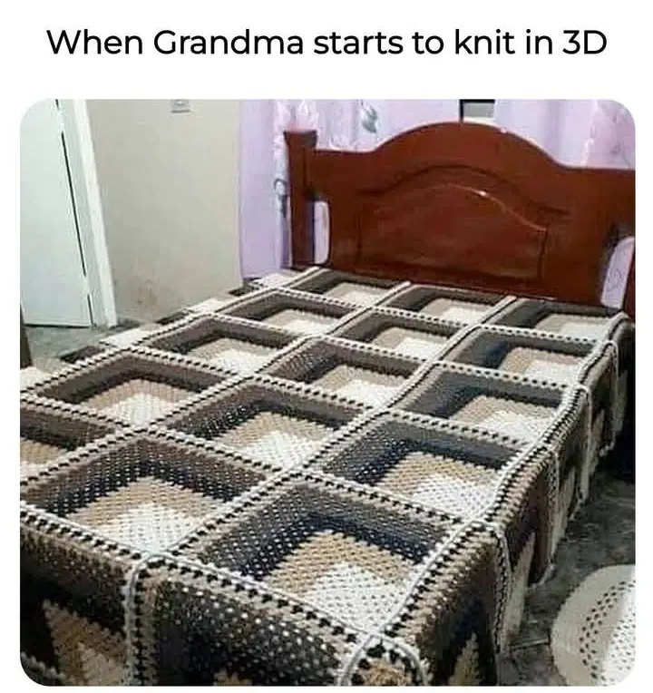 A bed covered with a crocheted blanket that forms a grid of raised, box-like 3D squares, creating a textured, geometric…