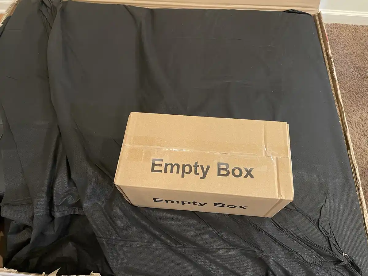 A plain brown cardboard box labeled 'Empty Box' in black text sits inside a larger open cardboard box filled with black…