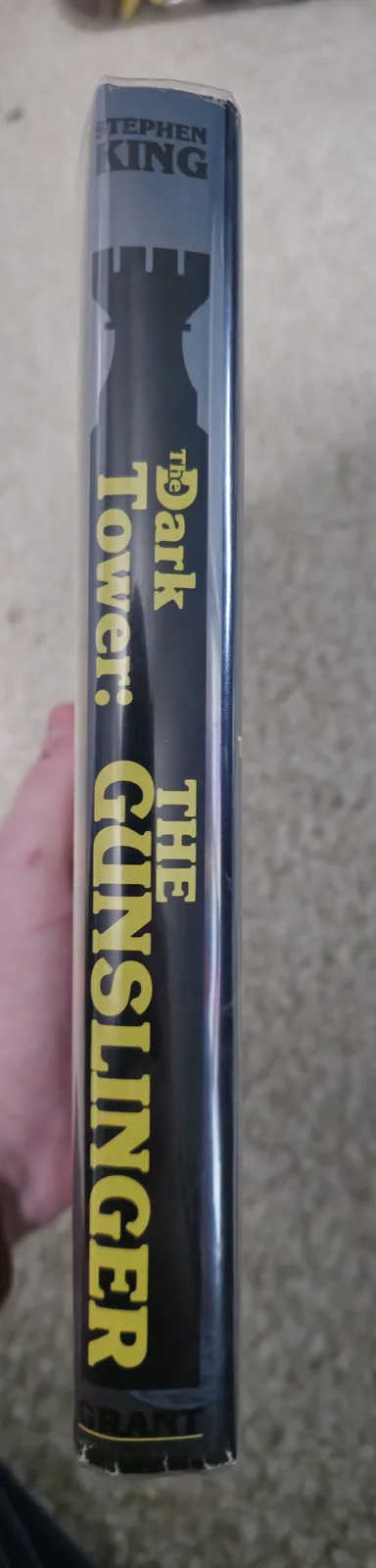 A close-up shot of the spine of a Stephen King book titled 'The Dark Tower: The Gunslinger,' held upright by a hand against…