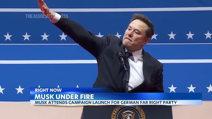 A man in a dark suit and tie stands at a podium with a seal, raising his right arm in a gesture resembling a salute. Behind…