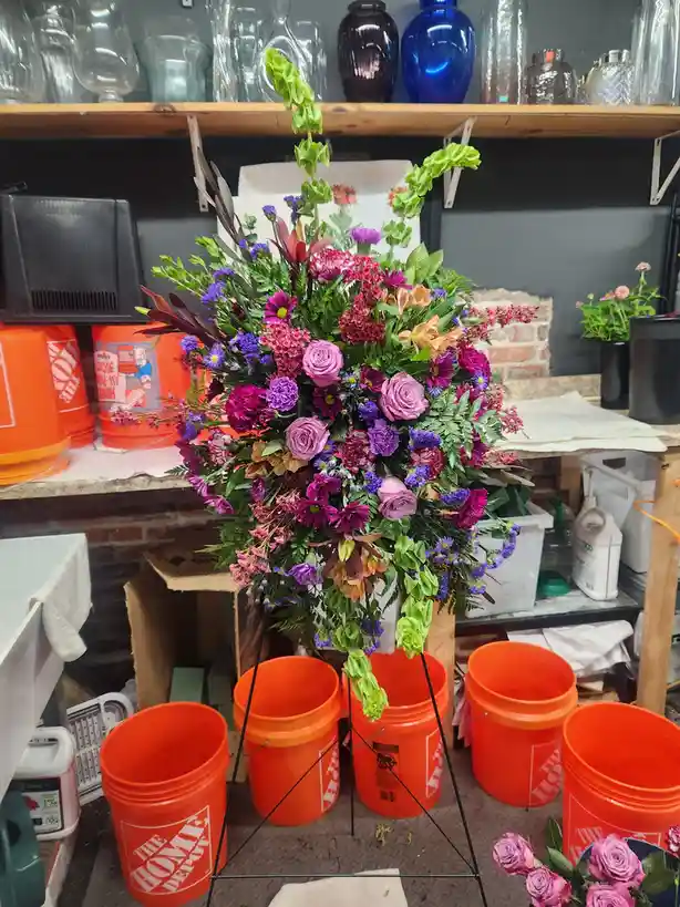 A large, colorful floral arrangement with pink, purple, and green flowers sits on a metal stand surrounded by several orange…