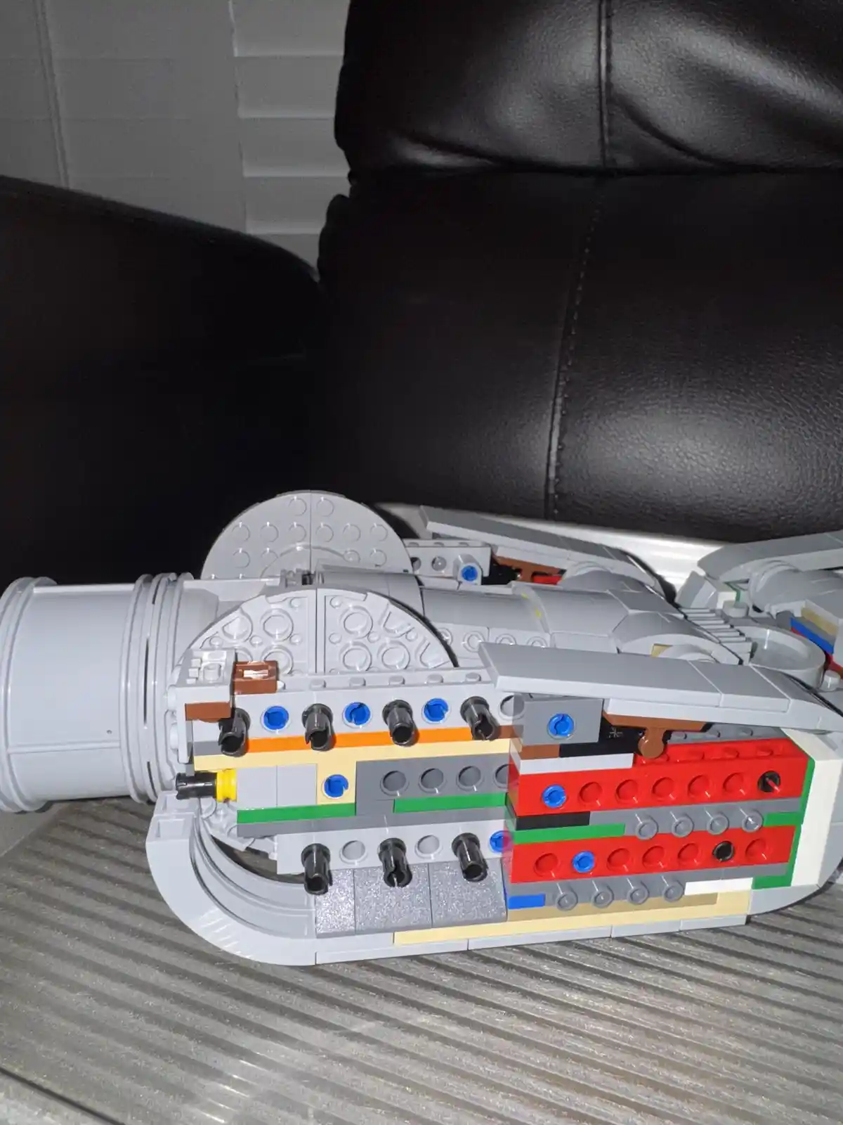 A partially assembled LEGO spaceship model, likely from a Star Wars set, is shown lying on its side on a textured gray…