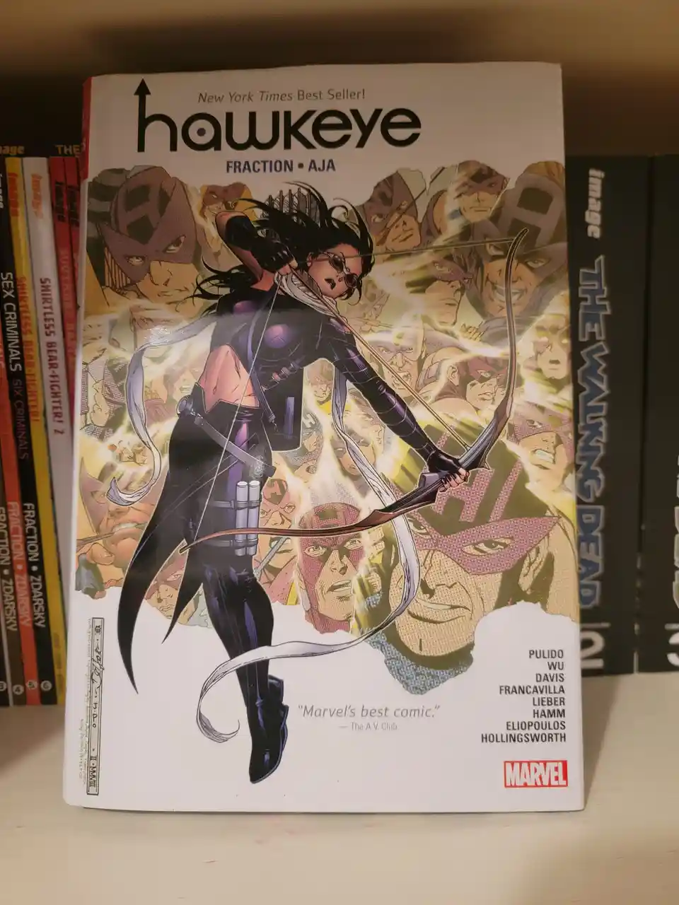 A comic book titled 'Hawkeye' by Fraction and Aja, featuring a female archer in a black suit aiming a bow, with a background…