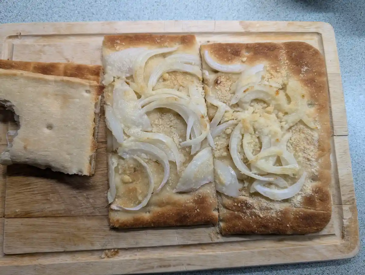 A wooden cutting board holds a rectangular flatbread cut into three pieces. The two right pieces are topped with sliced…