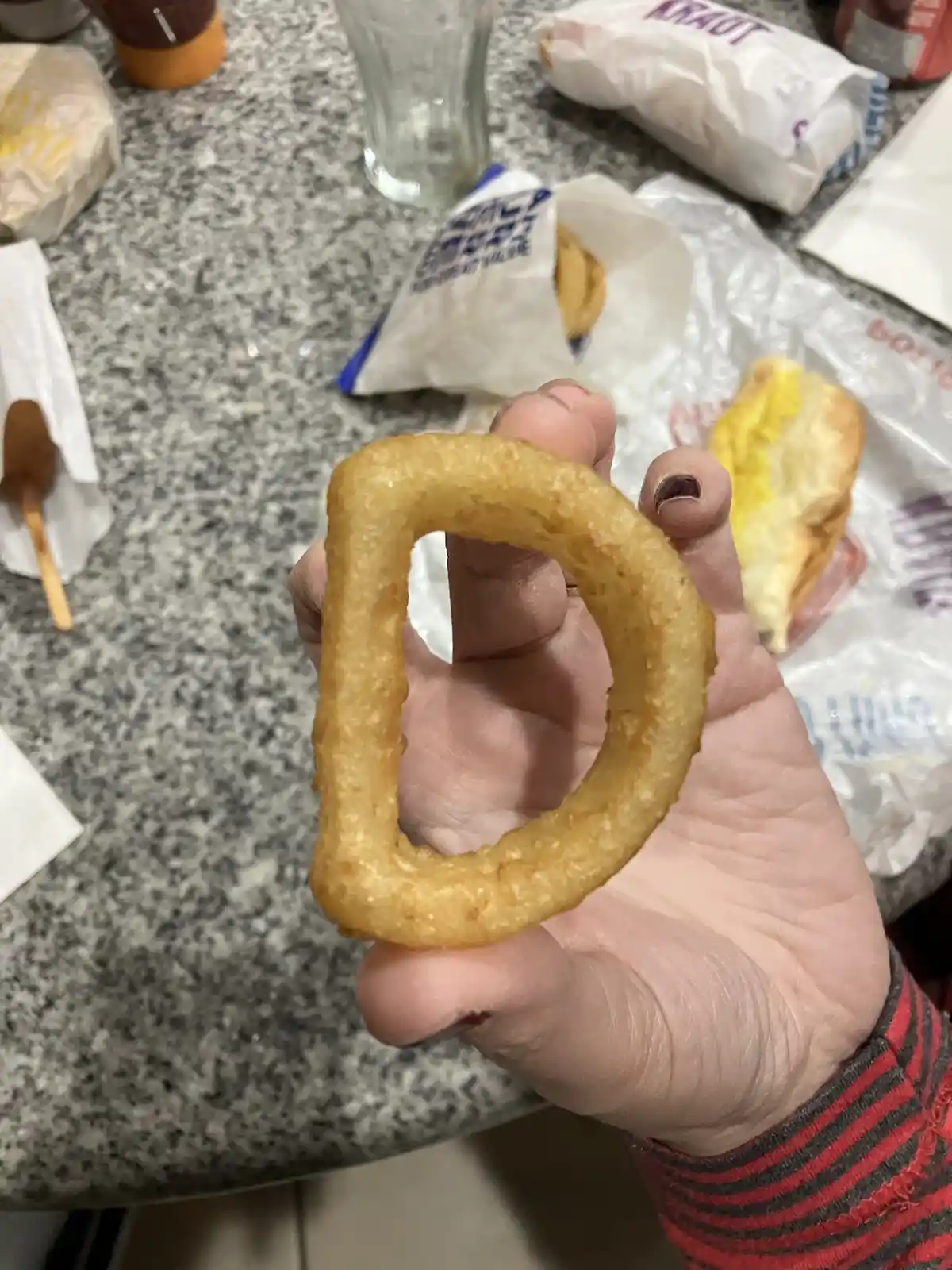 A hand holds a golden-brown, thickly battered fried food item, shaped like a distorted letter 'D' with a large, irregular…