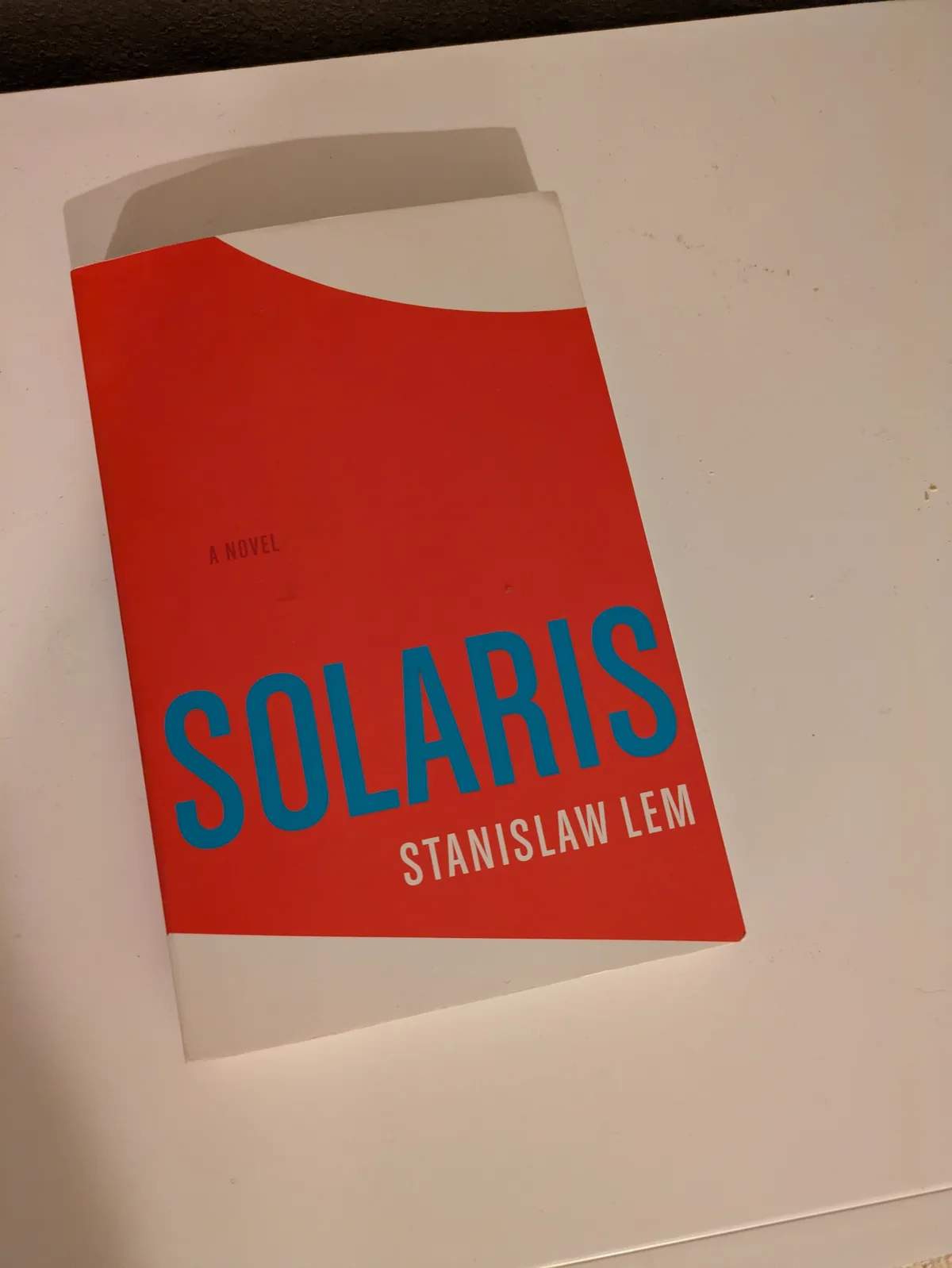 A physical copy of the book 'Solaris' by Stanislaw Lem, featuring a minimalist red and white cover with the title in large…