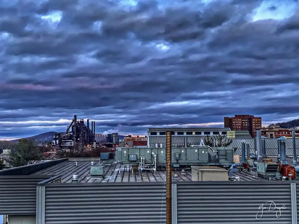 A rooftop view of industrial buildings under a dramatic, cloudy twilight sky, with overlaid text reading 'i'm not lazy, i'm…