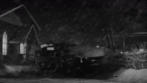 A black-and-white sequence of six frames from a classic film shows a vintage car stuck in heavy snow at night. In the first…