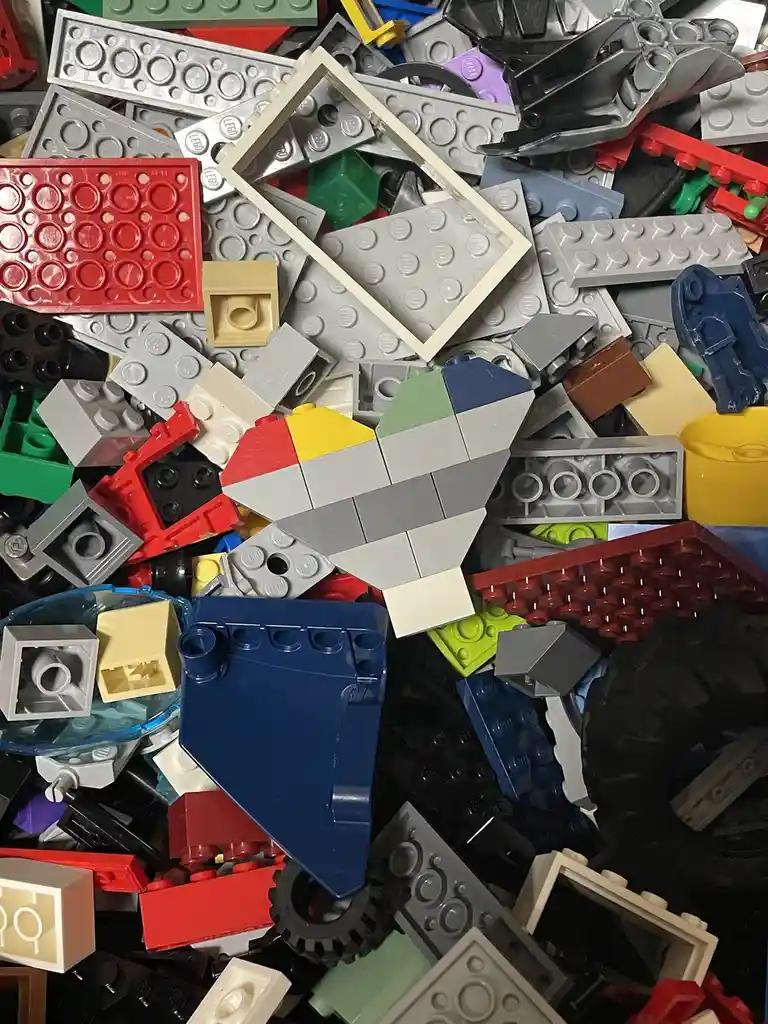 A pile of assorted colorful LEGO bricks and pieces, with a small heart shape constructed from gray, red, yellow, and green…