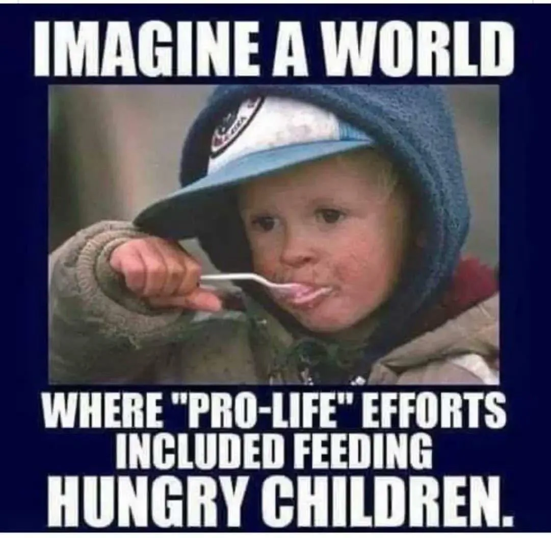 A young child wearing a blue hooded jacket and a baseball cap is shown eating from a spoon, with food smeared on their face…