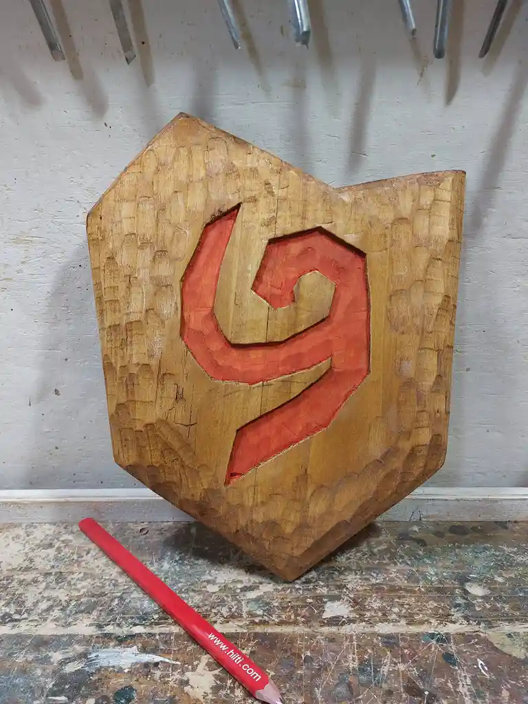 A wooden carving of the red Hilti logo, showing the stylized 'H' shape, is displayed on a workbench with a red pencil…