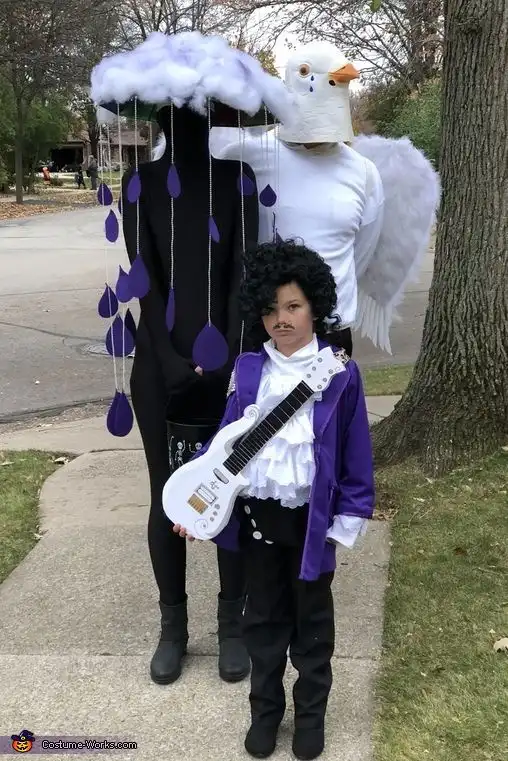 Three people in costumes stand outdoors: one as a dark cloud with purple raindrops, one as a white angel with wings, and a…