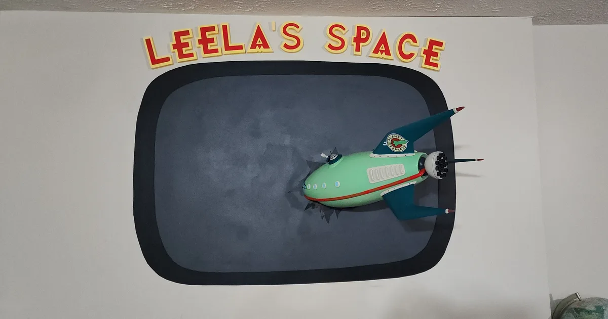 A wall decoration features a 3D cutout of a retro-style spaceship with a 'Planet Express' logo, set inside a black-bordered…