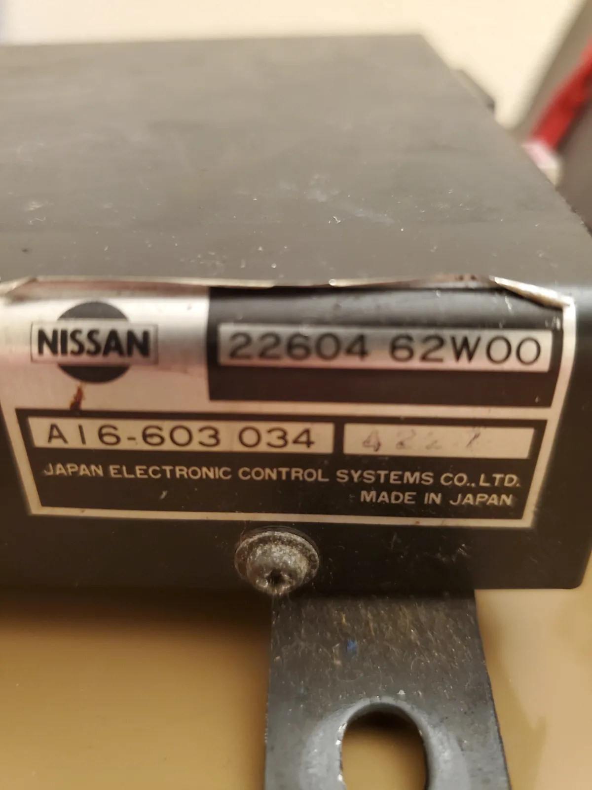 A close-up of a black Nissan electronic control module label showing part numbers and 'MADE IN JAPAN', with a handwritten…