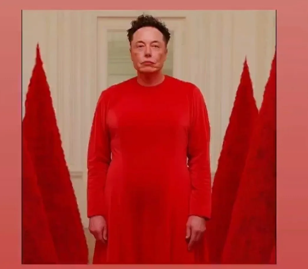 A man with dark hair stands in a plain red long-sleeved dress, flanked by two tall red triangular shapes resembling curtains…