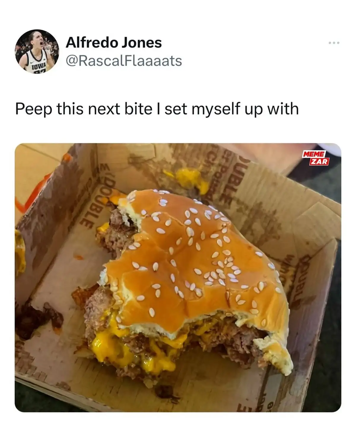 A partially eaten cheeseburger with a large bite taken out of it sits in a cardboard box, showing melted cheese and meat…
