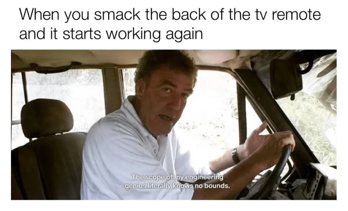 A man in a white shirt is driving a vehicle, looking at the camera with a smug expression while holding the steering wheel…