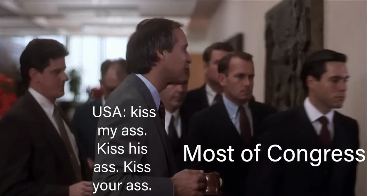 A still from a movie shows a man in a suit speaking to a group of men in suits. White text overlaid on the image reads 'USA…