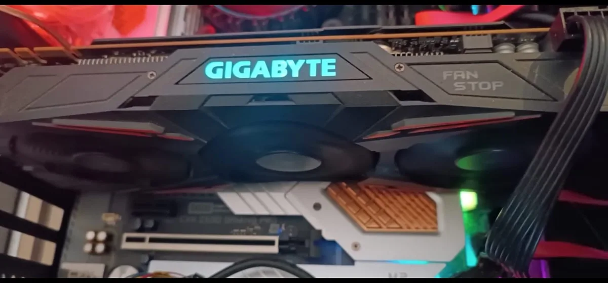 A close-up photo of a black Gigabyte graphics card with glowing blue 'GIGABYTE' branding and three fans, where the text 'FAN…