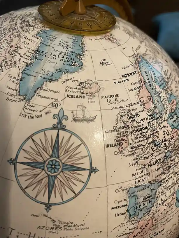 A close-up of a vintage-style globe showing the North Atlantic, with Iceland, Norway, and Western Europe visible. A…