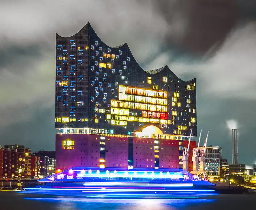 A nighttime photo of the Elbphilharmonie concert hall in Hamburg, Germany, with its distinctive glass and steel facade lit…