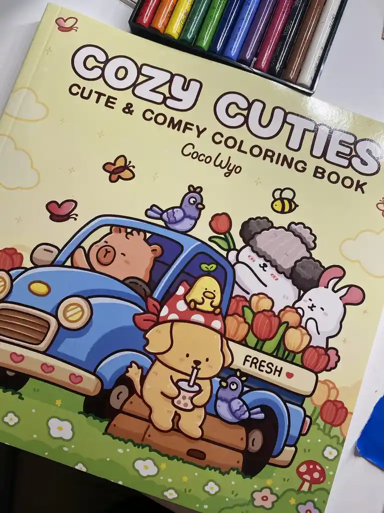 A close-up photo of a 'Cozy Cuties Cute & Comfy Coloring Book' by CocoWyo, featuring a cartoon cover with a blue car full of…