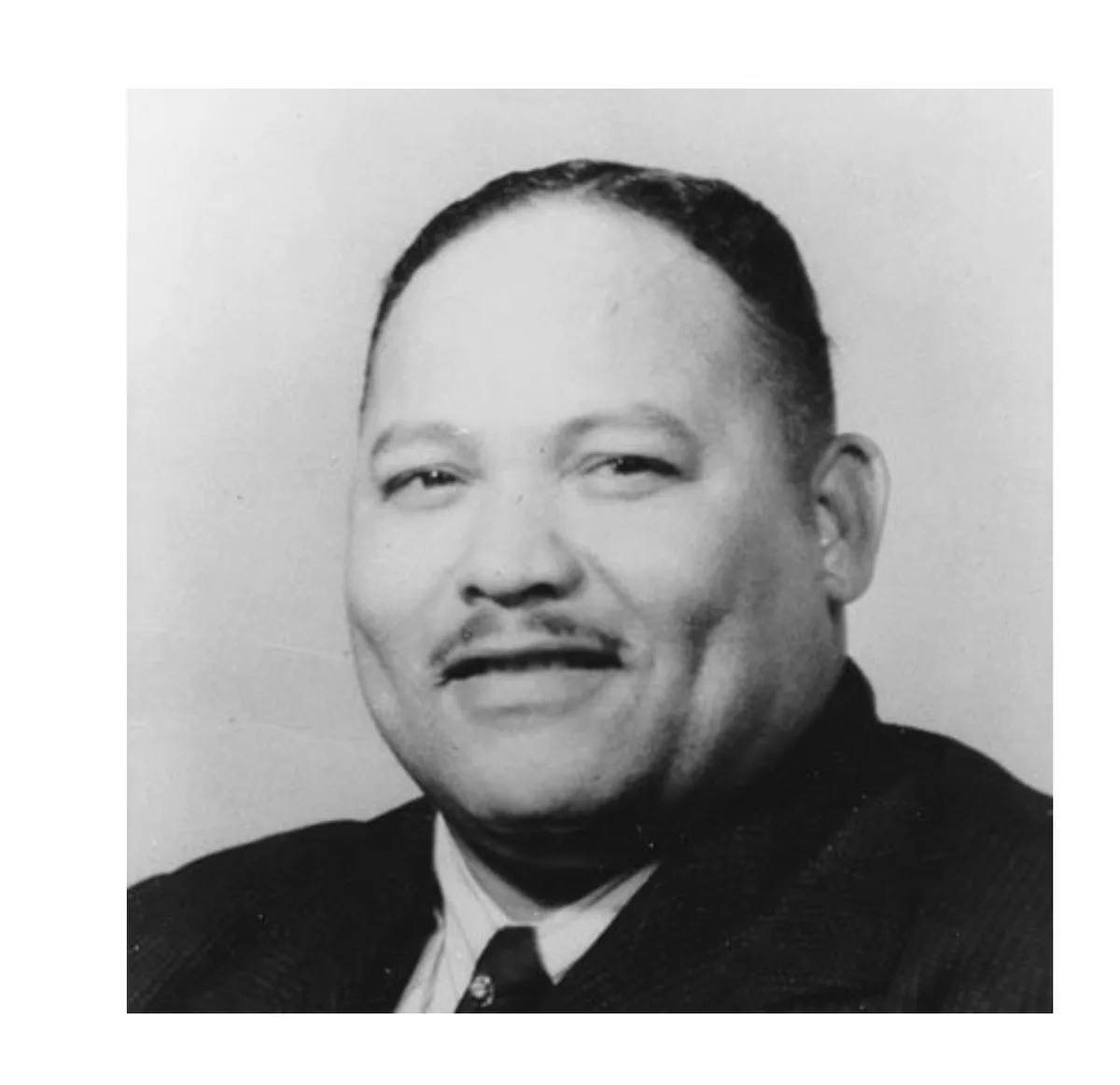 A black-and-white portrait of a smiling Black man in a suit and tie. Overlaid text reads: 'i'm not a racist, i'm just a…