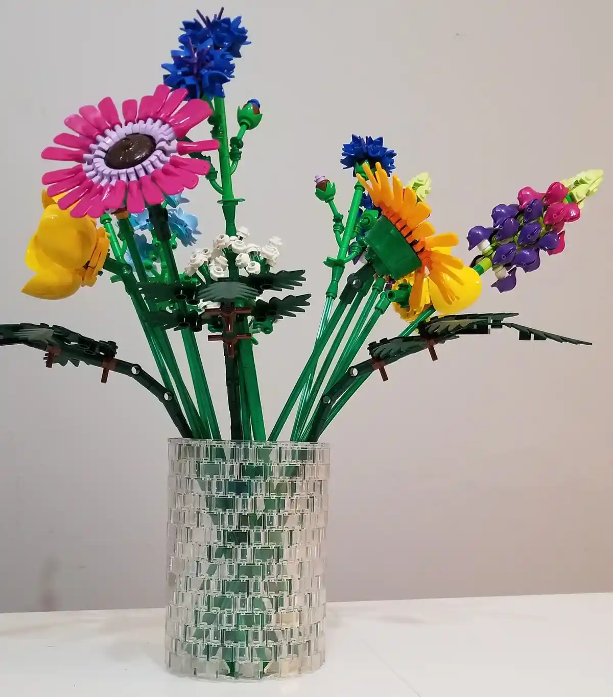 A colorful bouquet of flowers constructed entirely from LEGO bricks, featuring pink, blue, yellow, and purple blooms with…