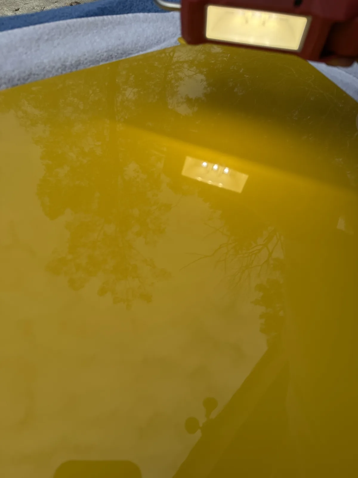 A close-up shot shows the glossy, yellow surface of a plastic tub or container, reflecting trees and a red lantern-like…