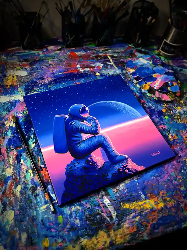A vibrant painting of a blue astronaut sitting alone on a rock, gazing at a planet against a starry sky, rests on a…